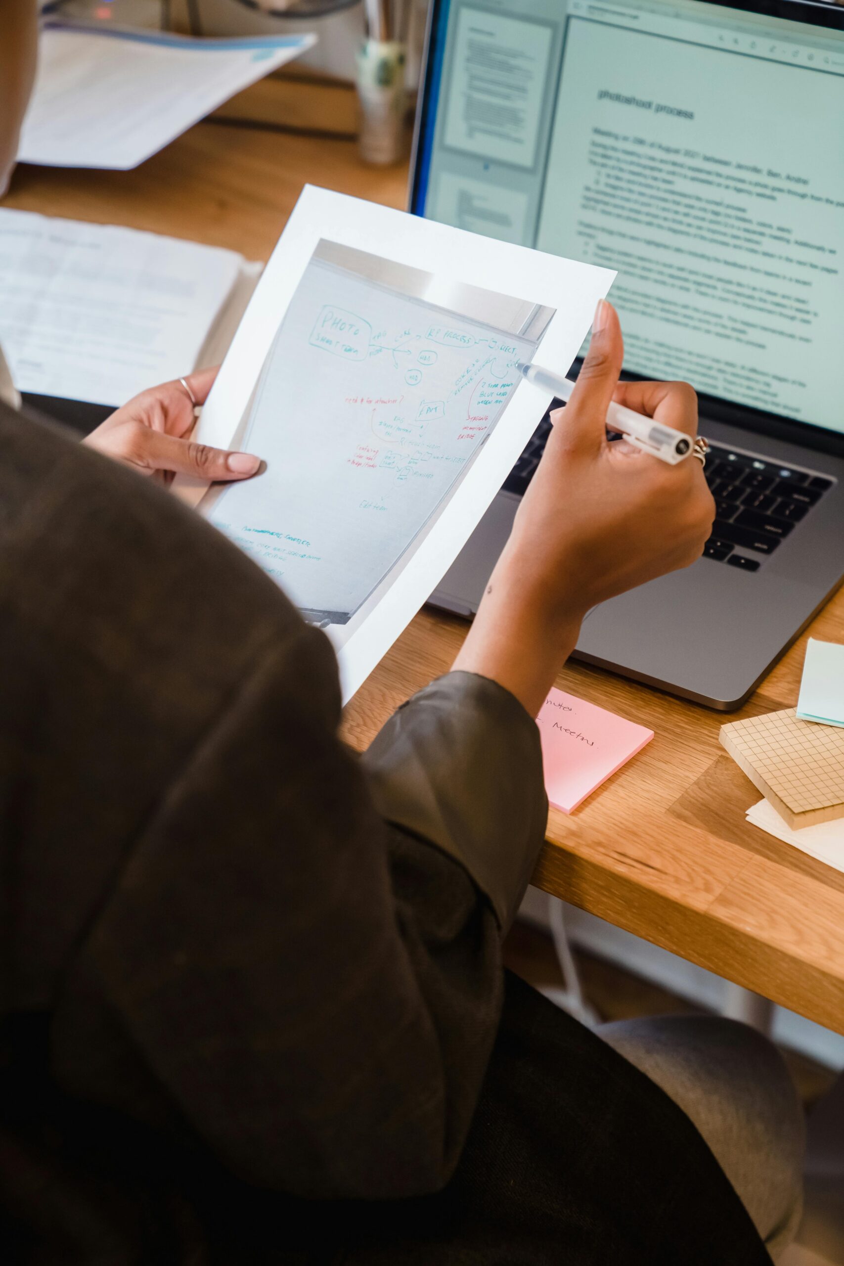 Woman reviewing printed documents at a desk with laptop, workspace tools visible.